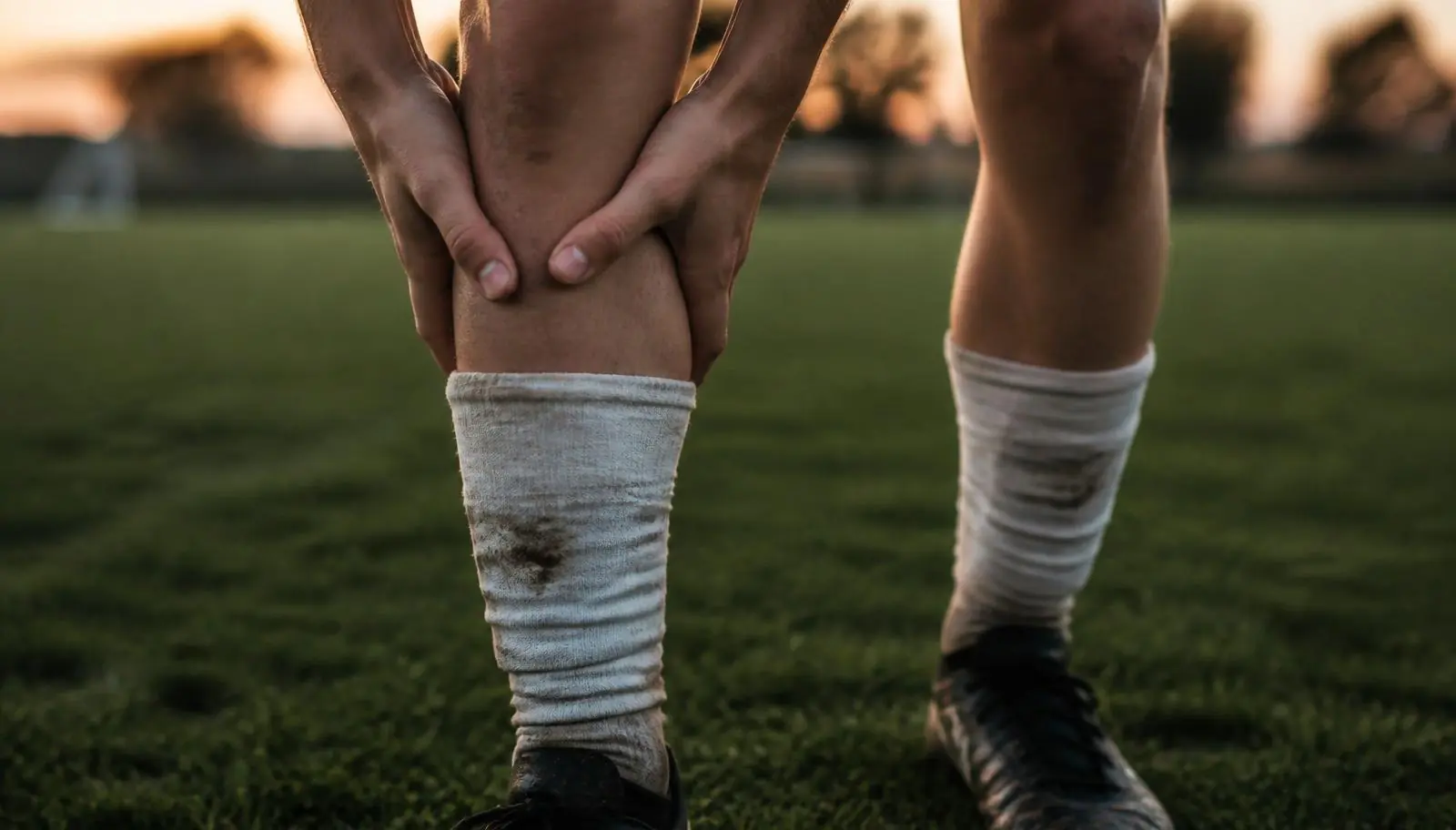 Ung fotbollsspelare i matchställ håller händerna strax under knäskålen på en gräsplan – typiskt smärtläge vid Schlatter